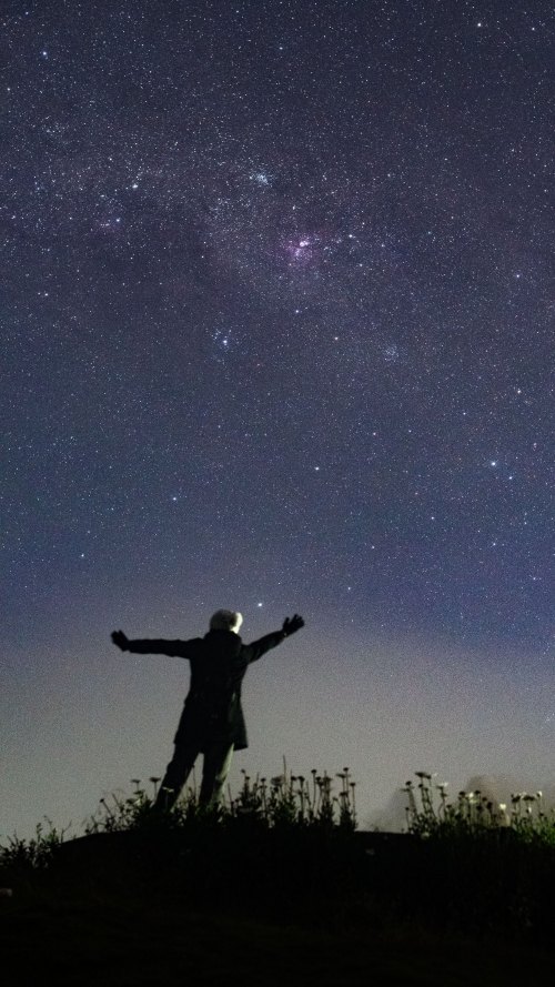 woman standing with her arms over her head looking up at the night sky full of stars